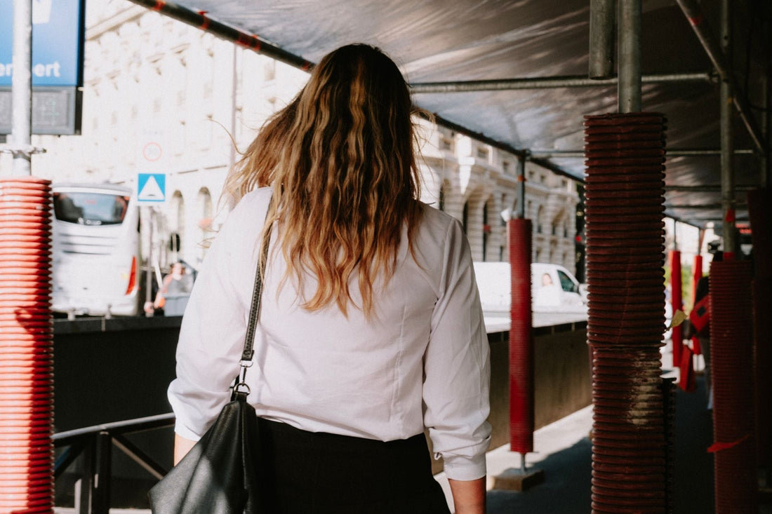 Rear view of woman in white shirt walking under scaffolding on a city street.