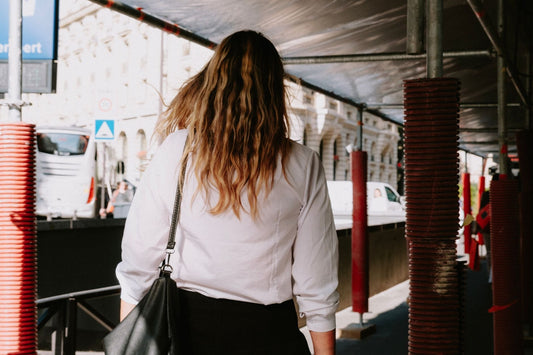 Rear view of woman in white shirt walking under scaffolding on a city street.