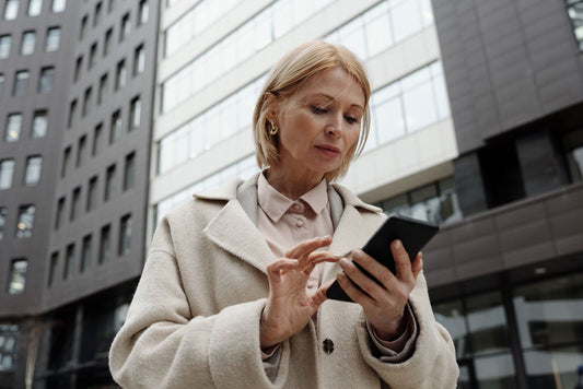 Woman in coat using smartphone in front of modern building. Professional and focused expression.