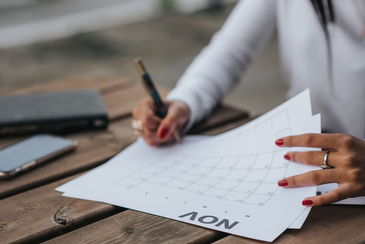Crop faceless female in white blouse making plans for month while sitting at wooden table in park