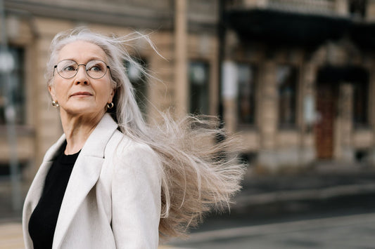 Stylish senior woman with flowing hair and eyeglasses walking in a breezy urban environment.