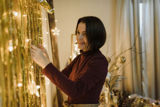 A woman decorates a room with gold streamers and lights, creating a festive ambiance.