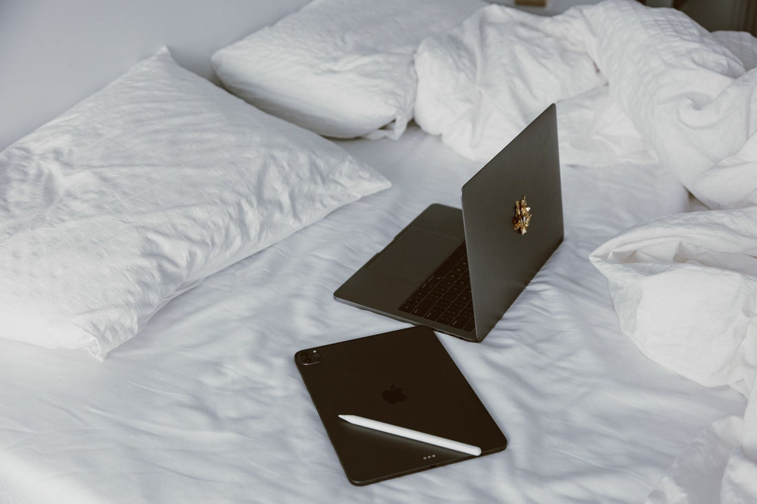A modern home office setup with a laptop and tablet on a white bed, perfect for remote work or leisure.