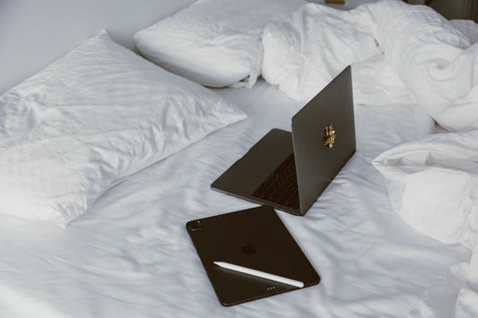A modern home office setup with a laptop and tablet on a white bed, perfect for remote work or leisure.